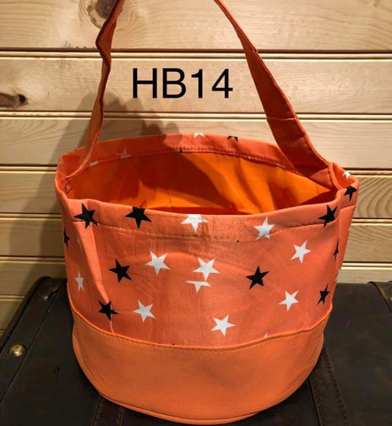 May include: Orange and white star patterned fabric trick or treat bag with black stars. The bag has a fabric handle and the text "HB14" is printed on the handle.