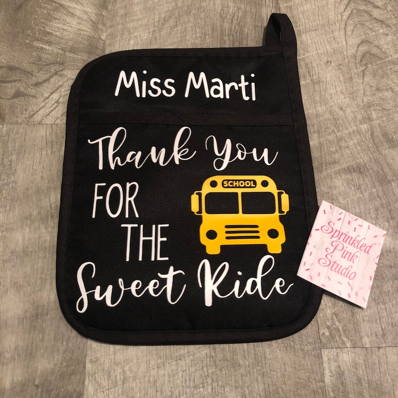 Puede incluir: Manopla de horno negra con texto blanco que dice "Miss Marti Thank You For The Sweet Ride" y un gr&aacute;fico de autob&uacute;s escolar amarillo. Una peque&ntilde;a etiqueta blanca con texto rosa que dice "Sprinkled Pink Studio" est&aacute; en la esquina inferior derecha.