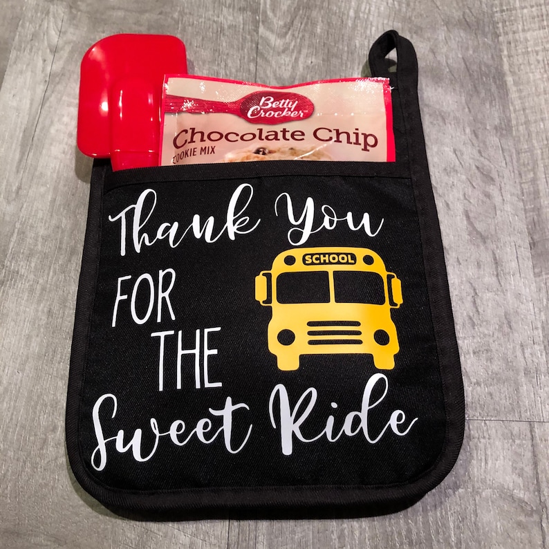 Black pot holder with white writing that says Thank You for the Sweet Ride and a yellow school bus on it. In addition a spoon and cookie mix can be purchased with the pot holder.