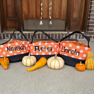 May include: Three orange and black Halloween trick-or-treat bags with white polka dots. The bags are labeled "Nevaeh", "Ace", and "Lincoln".
