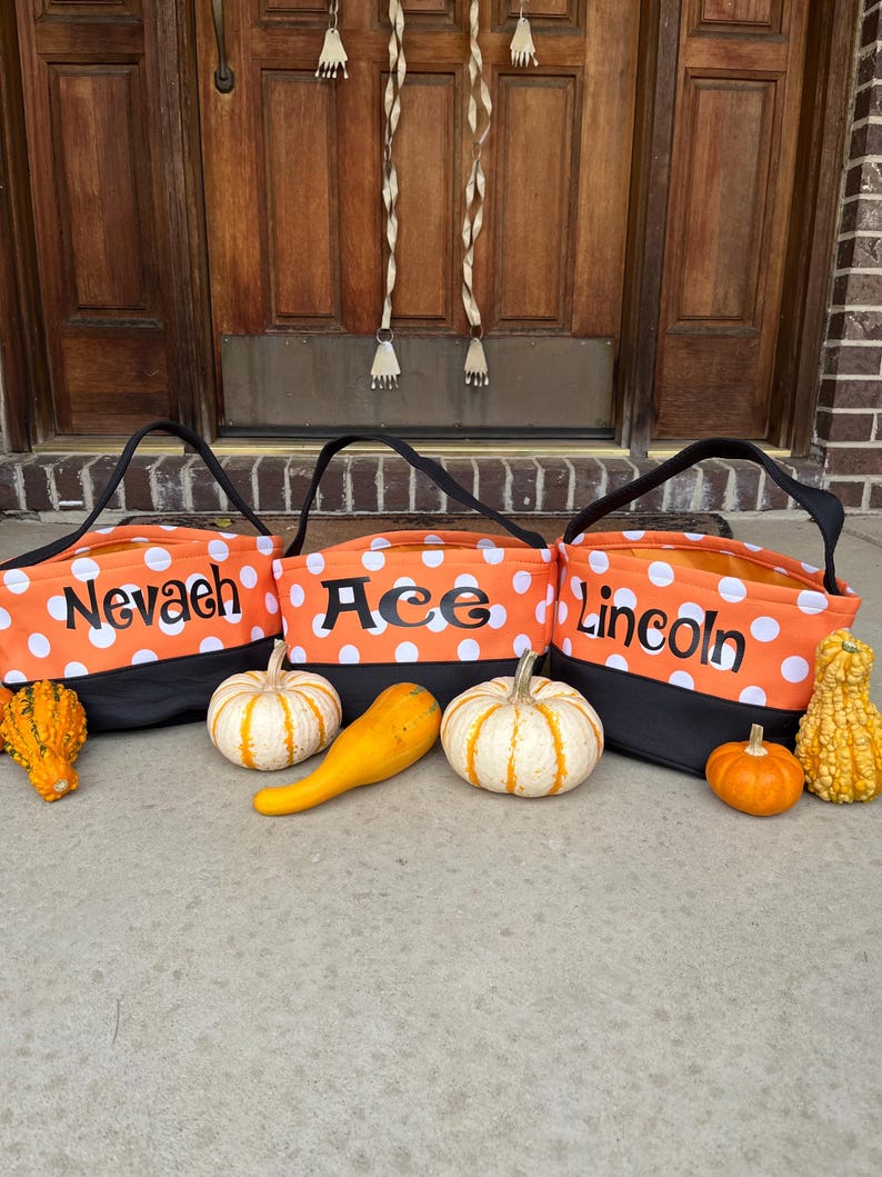 May include: Three orange and black Halloween trick-or-treat bags with white polka dots. The bags are labeled "Nevaeh", "Ace", and "Lincoln".