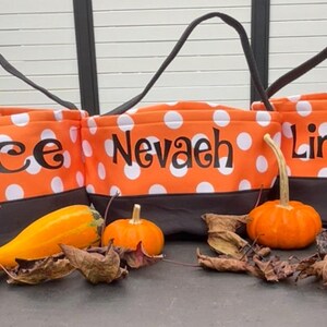 May include: Three orange and black Halloween trick-or-treat bags with white polka dots. The bags are personalized with the names "Ace", "Nevaeh", and "Lincoln".