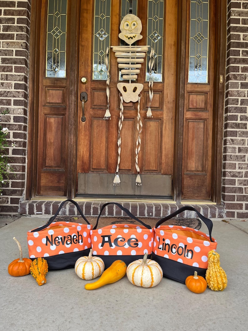 May include: Three orange and black Halloween trick-or-treat bags with white polka dots. The bags are personalized with the names "Nevaeh", "Ace", and "Lincoln".