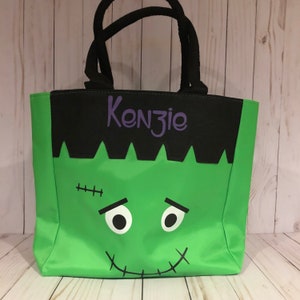 May include: Green and black Halloween trick or treat tote bag with a Frankenstein face and the name Kenzie in purple lettering.