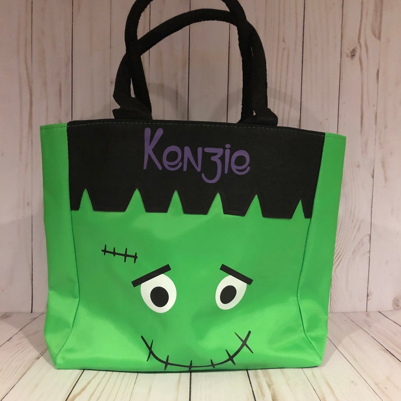 May include: Green and black Halloween trick or treat tote bag with a Frankenstein face and the name Kenzie in purple lettering.