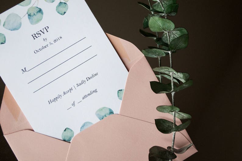 Op de afbeelding: Een roze envelop met een witte RSVP-kaart erin. De kaart heeft een aquarelontwerp met eucalyptusbladeren en de tekst "RSVP v&oacute;&oacute;r 5 oktober 2018".