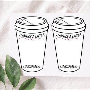 Puede incluir: Dos pegatinas blancas de tazas de café con contornos negros. Cada taza tiene una tapa y el texto "THANKS A LATTE" en negro con un corazón rosa y una línea rosa. La palabra "HANDMADE" está impresa en negro en la parte inferior de cada taza.