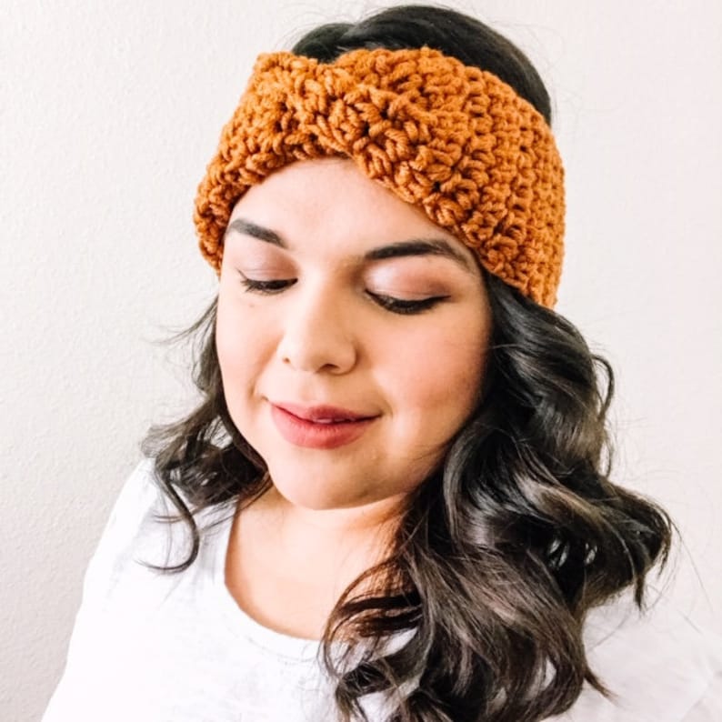 May include: A brown crocheted headband with a twisted design. The headband is worn by a person with long, dark hair.