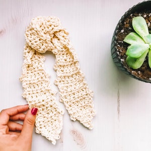 Pode incluir: Um len&ccedil;o de cabelo de cor creme em croch&ecirc; com um design de n&oacute;. O len&ccedil;o &eacute; feito de um fio macio e texturizado e tem um visual delicado e feminino.