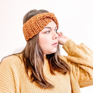 May include: A brown crocheted headband with a twisted design. The headband is worn by a person with long brown hair and a yellow sweater.
