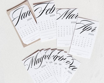 Può includere: Una collezione di piccoli calendari bianchi del 2026, ognuno con un mese diverso. I nomi dei mesi sono scritti in un'elegante grafia nera. I calendari sono disposti su una superficie bianca.