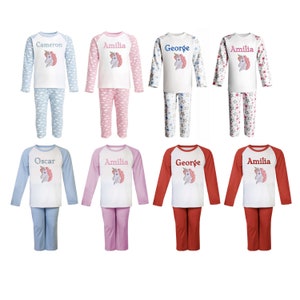May include: Eight pairs of children's pajamas with a unicorn design. The pajamas are in various colors, including blue, pink, red, and white. The pajamas have different patterns, including stars, clouds, and polka dots. The pajamas are personalized with names, including Cameron, Amilia, George, and Oscar.