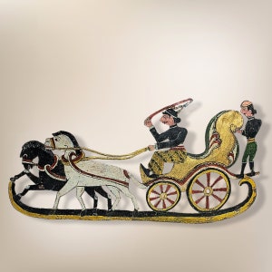 Può includere: Un burattino d'ombra dipinto a mano che rappresenta un carro trainato da due cavalli. Il carro è dorato con accenti rossi e neri. L'auriga indossa un abito nero e giallo e un cappello rosso. Una seconda figura in un abito verde e nero si trova dietro il carro.