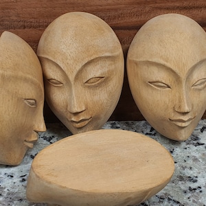 Puede incluir: Tres máscaras de madera con rasgos faciales tallados. Las máscaras son de color marrón claro y tienen un acabado liso y pulido.