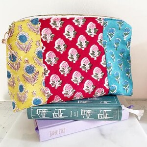 May include: A patchwork makeup bag with a zipper closure. The bag is made of three different fabrics with floral patterns in yellow, pink, and blue.