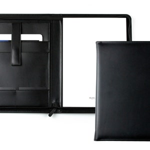 Op de afbeelding: Zwarte lederen portfoliomap met een ritssluiting, meerdere vakken en een ingebouwde penhouder. De map is open en laat een blanco witte pagina zien.