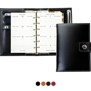 May include: Black leather bound planner with a pen, card slots, and a weekly and monthly calendar view. The planner has a flap closure with a button.