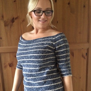 May include: A blue and white striped off-the-shoulder sweater with a slightly loose fit. The sweater is made of a soft, textured fabric.