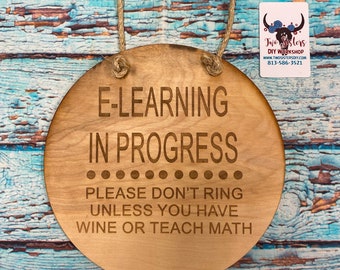 May include: A round wooden sign with the text "E-LEARNING IN PROGRESS PLEASE DON'T RING UNLESS YOU HAVE WINE OR TEACH MATH" engraved on it. The sign is hanging from a rope.