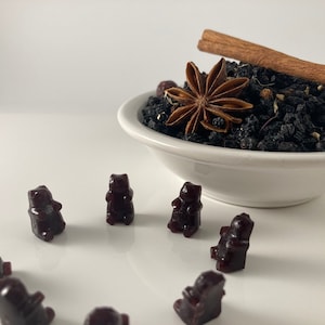 Könnte beinhalten: Eine weiße Schüssel gefüllt mit schwarzen Teeblättern, Sternanis und einem Zimtstange.  Um die Schüssel herum liegen acht dunkelviolette Gummibärchen.