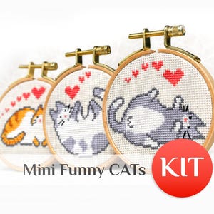 May include: Three cross-stitch kits featuring cartoon cats in wooden hoops. The cats are in various poses, with red hearts above them. The text "Mini Funny CATS KIT" is below the hoops.