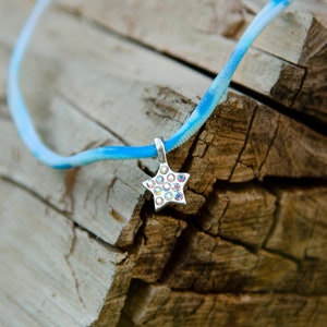 May include: A blue and white striped cord necklace with a silver star charm. The star is covered in clear rhinestones.