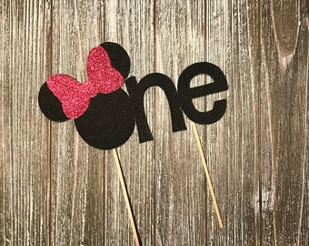 May include: Black and red glitter cake topper with the word "one" and a Minnie Mouse head with a bow.