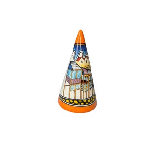 May include: A ceramic cone-shaped ring holder with a colourful painted design of a building with blue, pink, yellow, and green accents. The base of the holder is orange with black dots.