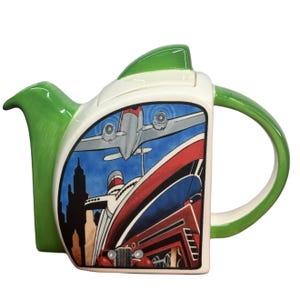 May include: A green and white ceramic teapot featuring a colourful illustration of a plane, a ship, and a car. The teapot has a lid and a handle.