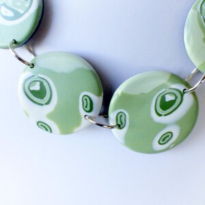 May include: A necklace made of green and white marbled round beads connected by silver rings.