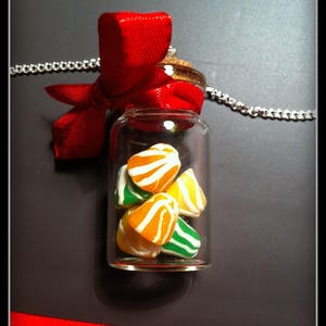 May include: A glass bottle necklace with a red ribbon and a silver chain. The bottle contains small, colorful candies with orange, green, and white stripes.