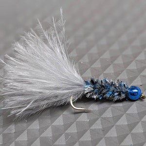 May include: A black and blue fly fishing lure with a white feather tail and a blue bead.