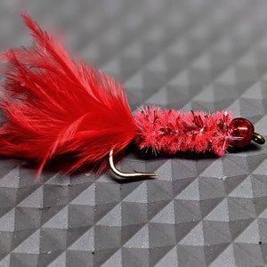 May include: A red and gold fly fishing lure with a red feather tail and a red chenille body.