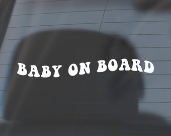 May include: White vinyl sticker with the text "BABY ON BOARD" in a retro font style. The sticker is on a car window.