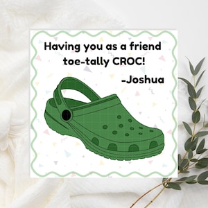 May include: A green Croc shoe illustration on a white background with the text "Having you as a friend toe-tally CROC! -Joshua". The image has a decorative border and colorful geometric shapes.