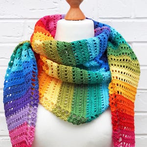 Puede incluir: Un chal de ganchillo arcoíris con un patrón de encaje. El chal está drapeado sobre un maniquí blanco.