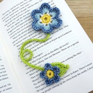 May include: Two crocheted blue flowers with yellow centres and green stems. The flowers are on a book with text.