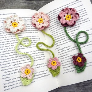 May include: A crocheted bookmark with multiple pink, red, and green flowers. The bookmark is attached to a book with the text "THE SECRET COMMONWEALTH" visible.