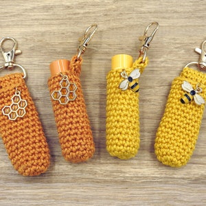 Pode incluir: Quatro chaveiros de crochê com pingentes de abelha e favo de mel. Os chaveiros são amarelos e laranja e são feitos com um ponto de crochê texturizado.