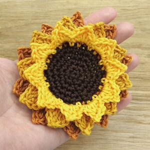 May include: A crocheted sunflower with yellow and orange petals and a brown center.