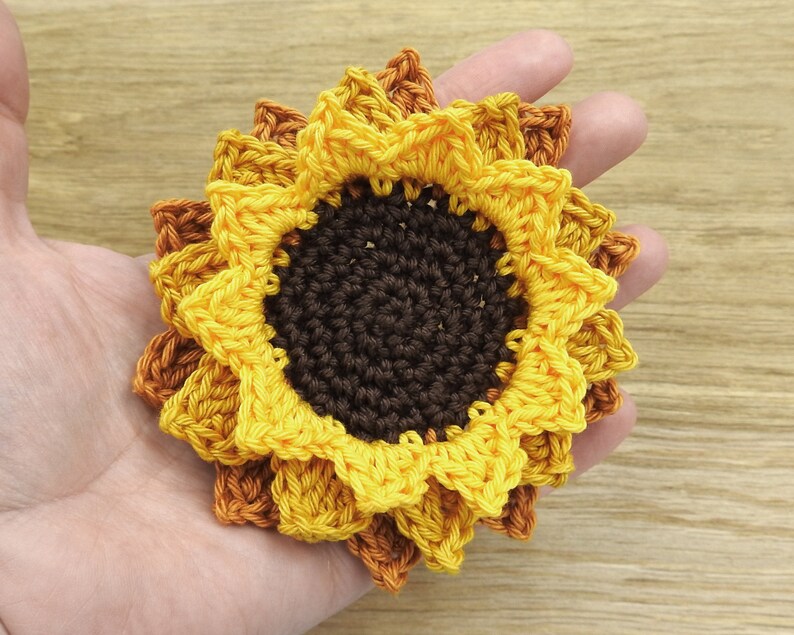 May include: A crocheted sunflower with yellow and orange petals and a brown center.