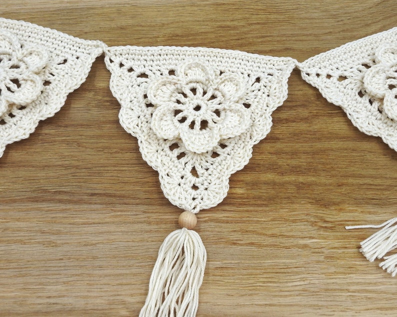May include: A white crocheted garland with a flower design and wooden beads. The garland has tassels on each end.