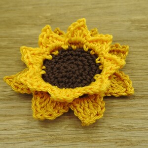 May include: A crocheted sunflower with yellow petals and a brown center.