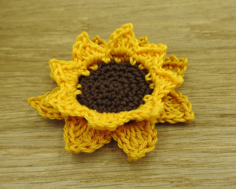 May include: A crocheted sunflower with yellow petals and a brown center.
