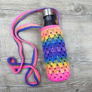 May include: A rainbow crocheted water bottle holder with a silver water bottle inside. The holder is made of a colorful yarn with a pink, purple, blue, green, yellow, and orange color scheme.