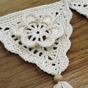 May include: A white crocheted banner with a flower design and a wooden bead tassel.