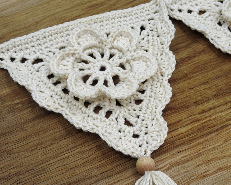 May include: A white crocheted banner with a flower design and a wooden bead tassel.