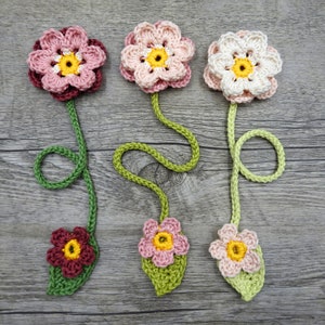 May include: Three crocheted flower bookmarks with green stems and leaves. The flowers are pink, white, and red with yellow centers.