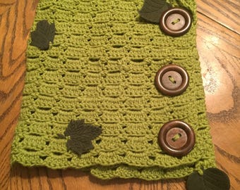 May include: A green crocheted scarf with brown buttons and green felt leaves.