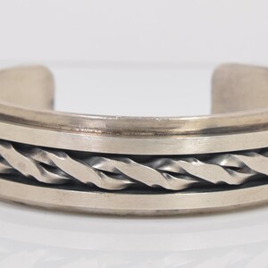 May include: Silver-toned cuff bracelet with a braided rope design in the center. The bracelet has a simple, elegant design with a polished finish. The open cuff design allows for easy wear.